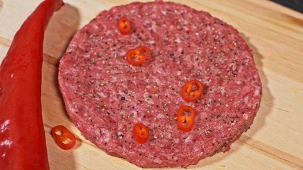 Cook makes meat medallions for burgers. Chef in black food gloves makes cutlet. Cutlets are leveled in steel ring in an even medallion. On top of pouring spices pepper and salt.