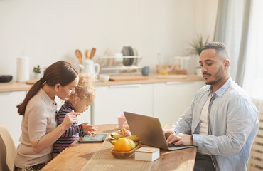 Side view portrait of modern father using laptop while enjoying family breakfast in cozy kitchen interior