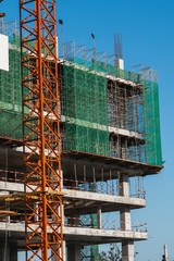 Crane and building construction site against blue sky. Metal construction of unfinished building on construction. Tower Crane use for building of multi storage building.