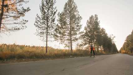 Training an athlete on the roller skaters. Biathlon ride on the roller skis with ski poles, in the helmet. Autumn workout. Roller sport. Adult man riding on skates.