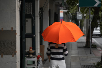 Back view of woman with orange umbrella walking on a street.