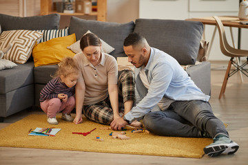 Full length portrait of happy modern family playing with cute little girl in cozy home interior, copy space