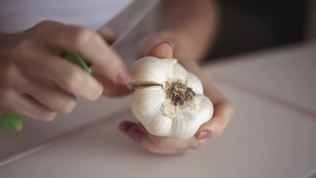 Young woman's hands peel fresh garlic head on white background