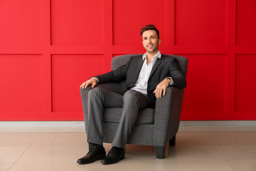 Handsome businessman sitting in armchair near color wall