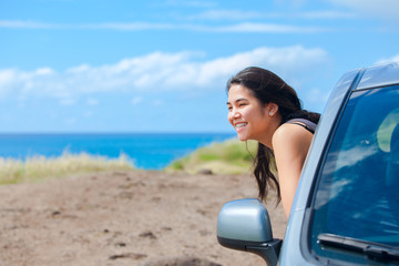 Smiling biracial teen girl leaning out car door by ocean