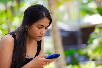 Biracial teen girl looking at cellphone in tropical setting