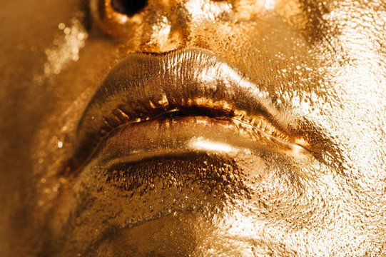 Close up image of woman lips, face covered with bright golden paint, makeup and beauty concept
