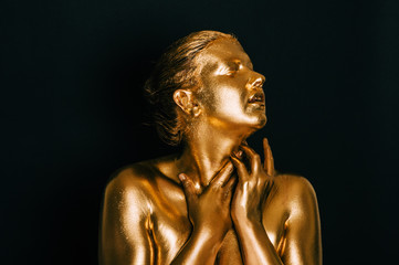 Portrait of sensual woman covered with golden paint, posing on black background, eyes closed