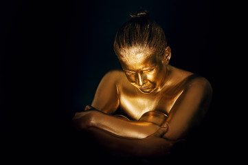 Portrait of sensual woman covered with golden paint, posing on black background, eyes closed, head down