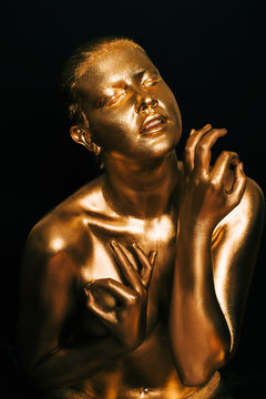 Portrait of sensual woman covered with golden paint, posing on black background, eyes closed