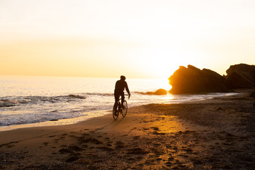 silhouette of young male bicycle rider in helmet on the beach during beautiful sunset