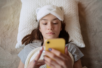 Cute teen girl woke up in the morning at home and using smartphone   