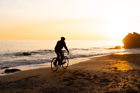 silhouette of young male bicycle rider in helmet on the beach during beautiful sunset