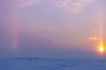 Winter evening landscape with snow-path, sun disk and a sunny halo in the sky. Natural winter background. Winter pink and blue sunset