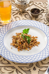 Tasty Pearl barley porridge with carrot and glass of yellow drink on oriental wooden table