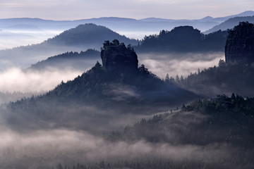 Kleiner Winterberg, morning view over sandstone cliff into deep misty valley in Saxony Switzerland, landscape in Germany. Fog and beautiful backlight. Stone hill sunset. Rocky landscape in Europe.
