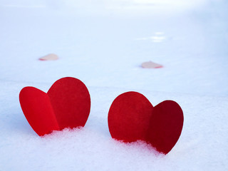 Fototapeta premium Red paper hearts on white snow as a symbol of love and warmth.