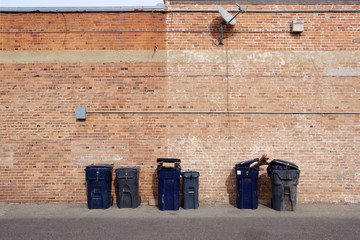 Close-up sectional full frame view of an old brick building side wall with a row of garbage bins