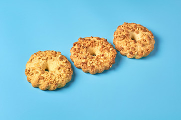 Row of three fresh circle oat cookies with hole and peanuts lies on blue desk on kitchen. Close-up