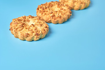 Row of three fresh circle oat cookies with hole and peanuts lies on blue desk on kitchen. Space for text