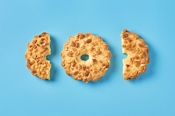 Row of whole and halves of fresh circle oat cookies with peanuts lies on blue desk on kitchen. Top view. Close-up