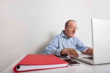 Senior businessman using laptop with book binder and cell phone on office desk