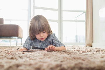 Boy using digital tablet while lying on rug in living room