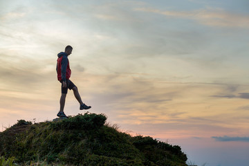 Dark silhouette of a hiker balancing on a summit stone in evening mountains.
