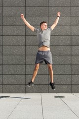 Full length of successful jogger jumping against tiled wall