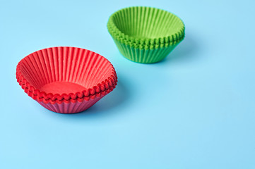 Two heaps of new red and green paper molds for baking muffins lies on blue desk on kitchen. Space for text
