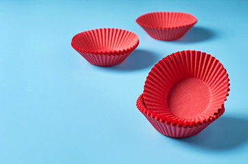 Scattered new red paper molds for baking muffins lies on blue desk on kitchen. Space for text
