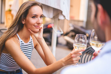 Smiling Woman toasting with white wine with her Man Sitting At Sidewalk Cafe