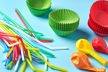 Different color paper molds for baking muffins, balloon and straw scattered on blue desk on kitchen. Close-up