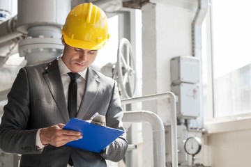Young male supervisor writing on clipboard in industry