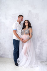 Fototapeta na wymiar Happy and attractive pregnant couple posing in studio. Husband tender hugging his wife