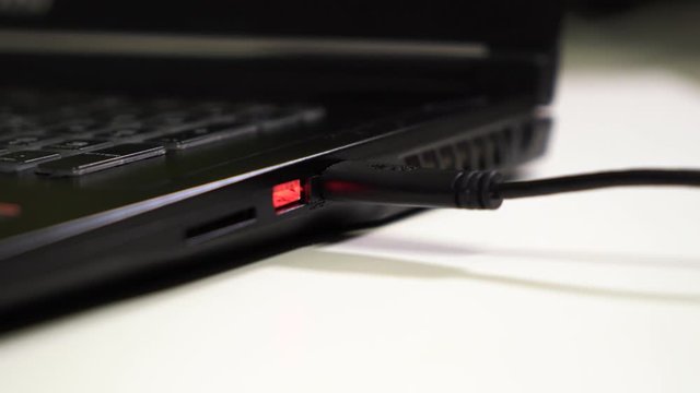 Close up male hand connect two black USB cable to laptop with glowing red usb port.