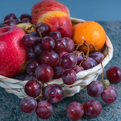 red grape berries and fresh fruits in a straw basket on a dark wooden background.