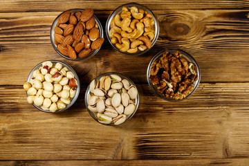Obraz na płótnie Canvas Assortment of nuts on wooden table. Almond, hazelnut, pistachio, walnut and cashew in glass bowls. Top view. Healthy eating concept