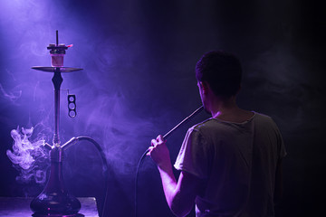 The man Smoking the classic Shisha. Beautiful background, with colored rays of light and smoke. The...