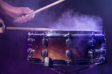 The drummer plays the drums. Beautiful blue and red background, with rays of light. Beautiful special effects smoke and lighting. Process of playing a musical instrument. Close-up photo.