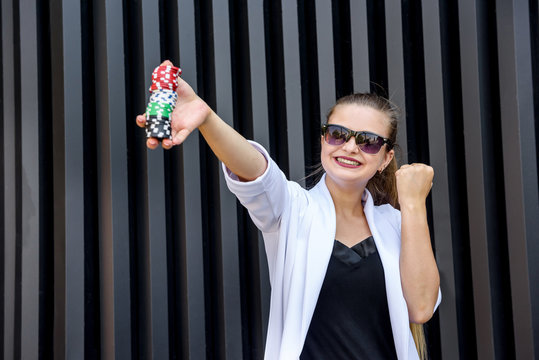 Gambling concept. Business woman in sunglasses holding poker chips and posing on abstract background