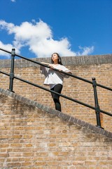 Low angle view of young woman looking away while leaning on railing against cloudy sky