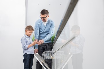 Father and son placing glass in dishwasher at kitchen