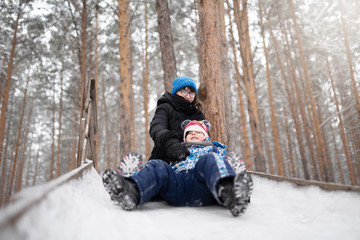 Fototapeta na wymiar mother and son sledding down the hill outdoors
