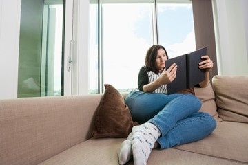 Obraz premium Full length of young woman reading book on sofa
