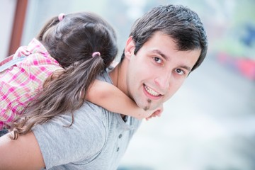 Side view portrait of young man piggybacking little daughter at home
