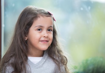 Portrait of cute little girl against glass window at home