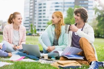 Young man having coffee while studying with female friends at college campus