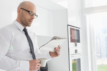 Fototapeta premium Mid adult businessman having coffee while reading newspaper at home