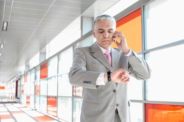 Middle aged businessman checking time while on call at railroad station